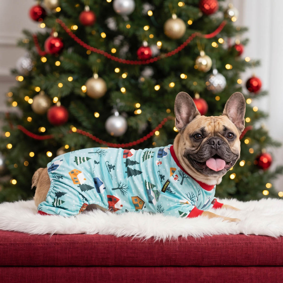 French bulldog lying on a white faux-fur rug in front of a decorated Christmas tree, wearing a light blue holiday dog pjs
