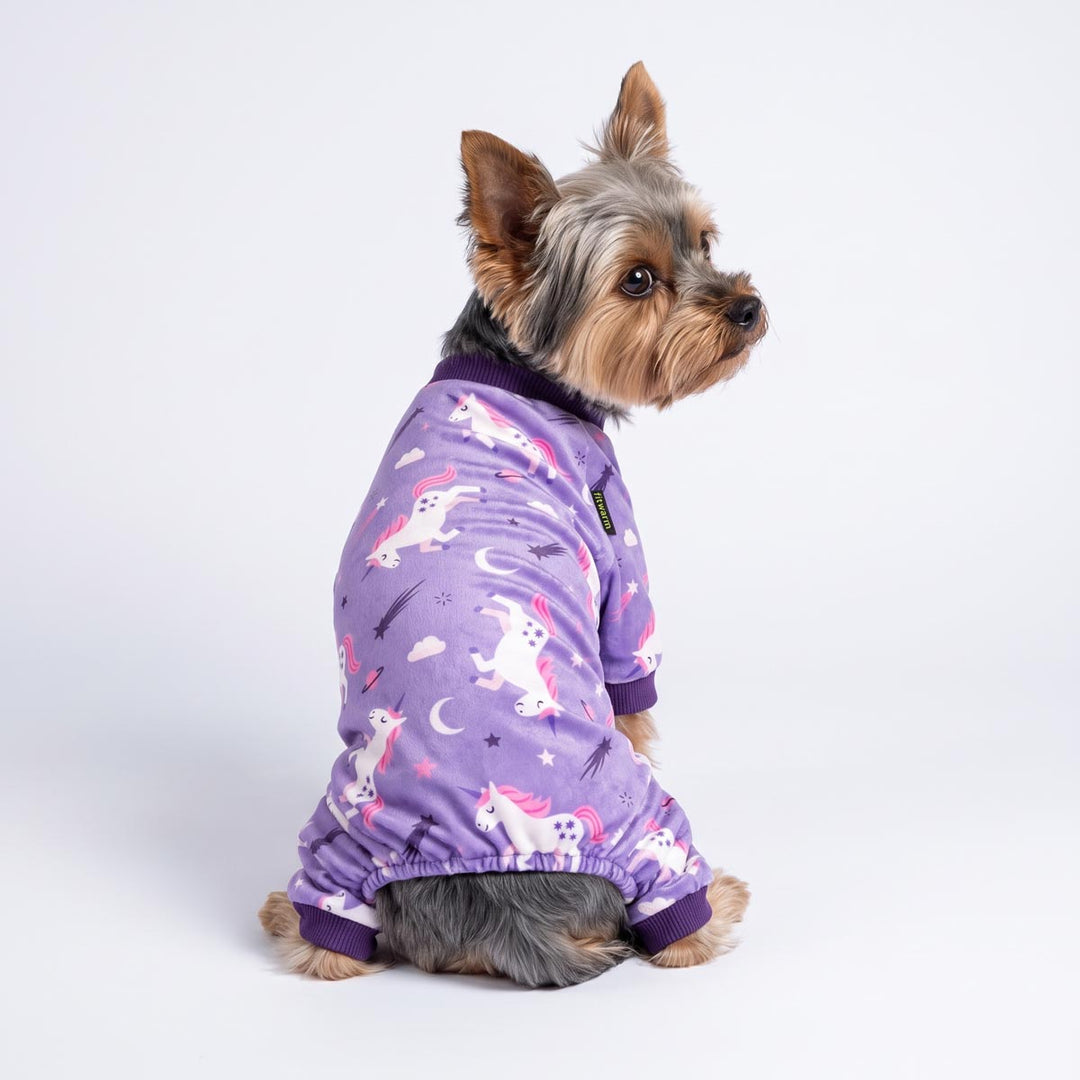 Small Yorkshire Terrier dog wearing a purple long-sleeve dog pjs with a white and pink unicorn pattern, photographed against a seamless white studio background