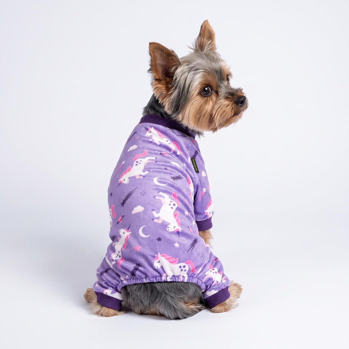 Small Yorkshire Terrier dog wearing a purple long-sleeve dog pjs with a white and pink unicorn pattern, photographed against a seamless white studio background