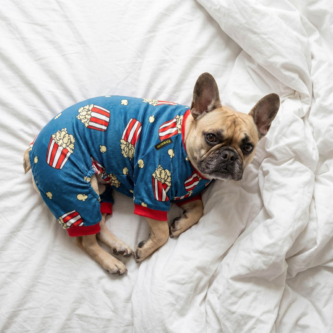French Bulldog wearing a dog fleece pajamas with popcorn prints and lying on the bed