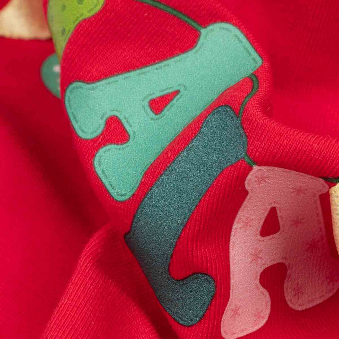 Close-up of a red fabric featuring large decorative letters in mint green, dark teal, and pale pink, with a small gold ribbon bow on the right
