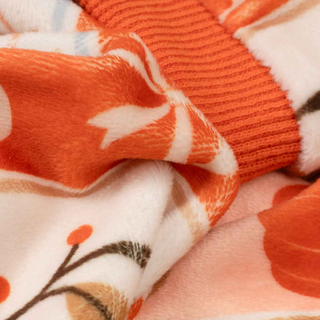 Close-up of a dog fleece pajamas with a warm orange and white patterned design, featuring a ribbed orange cuff and soft floral details