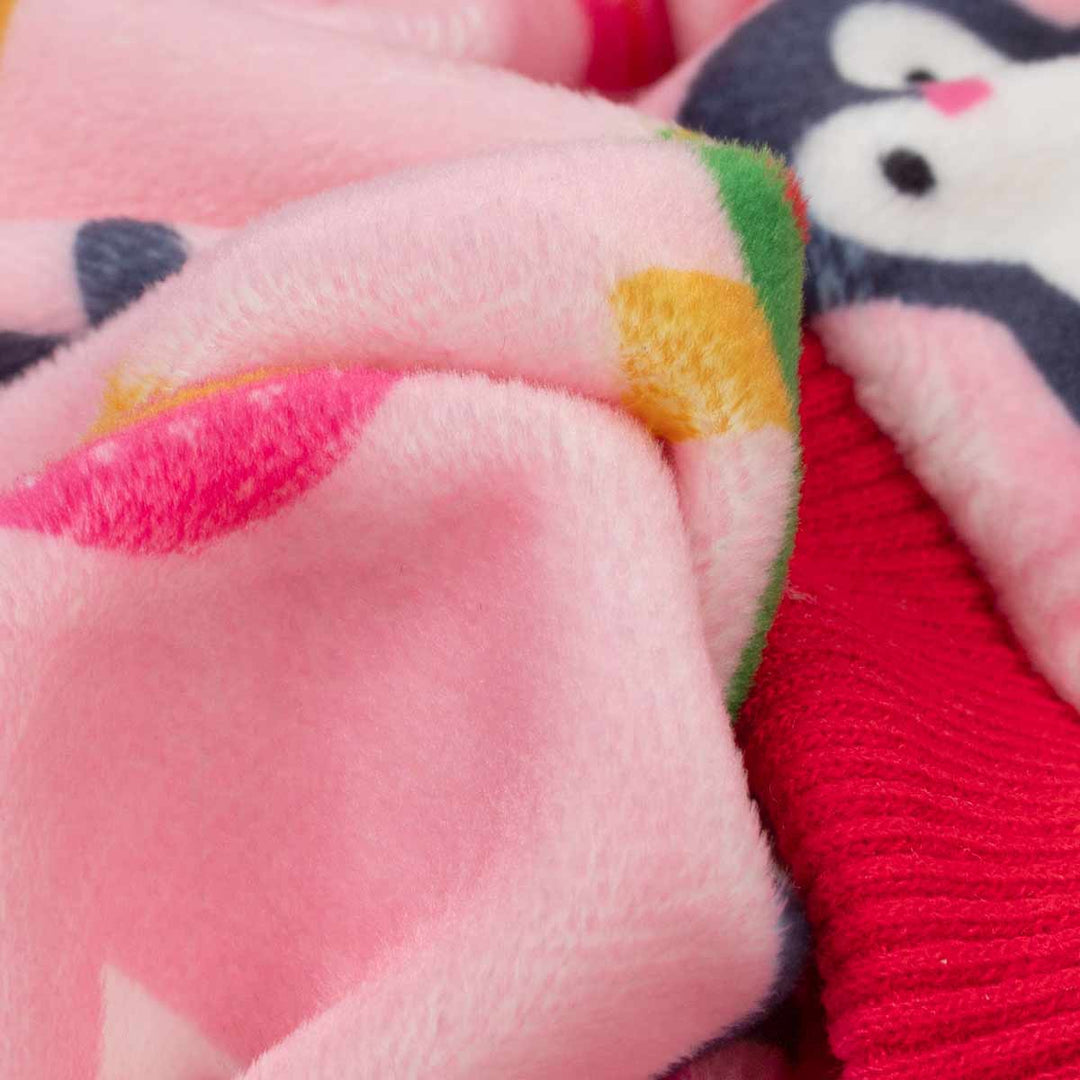 Close-up of a plush pink dog pajamas with colorful patches, layered over a red knit fabric and a penguin-patterned textile