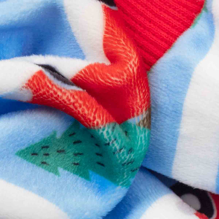 Close-up of a dog fleece pajamas with a colorful winter pattern featuring light blue and white stripes, a red textured section, and a green tree motif
