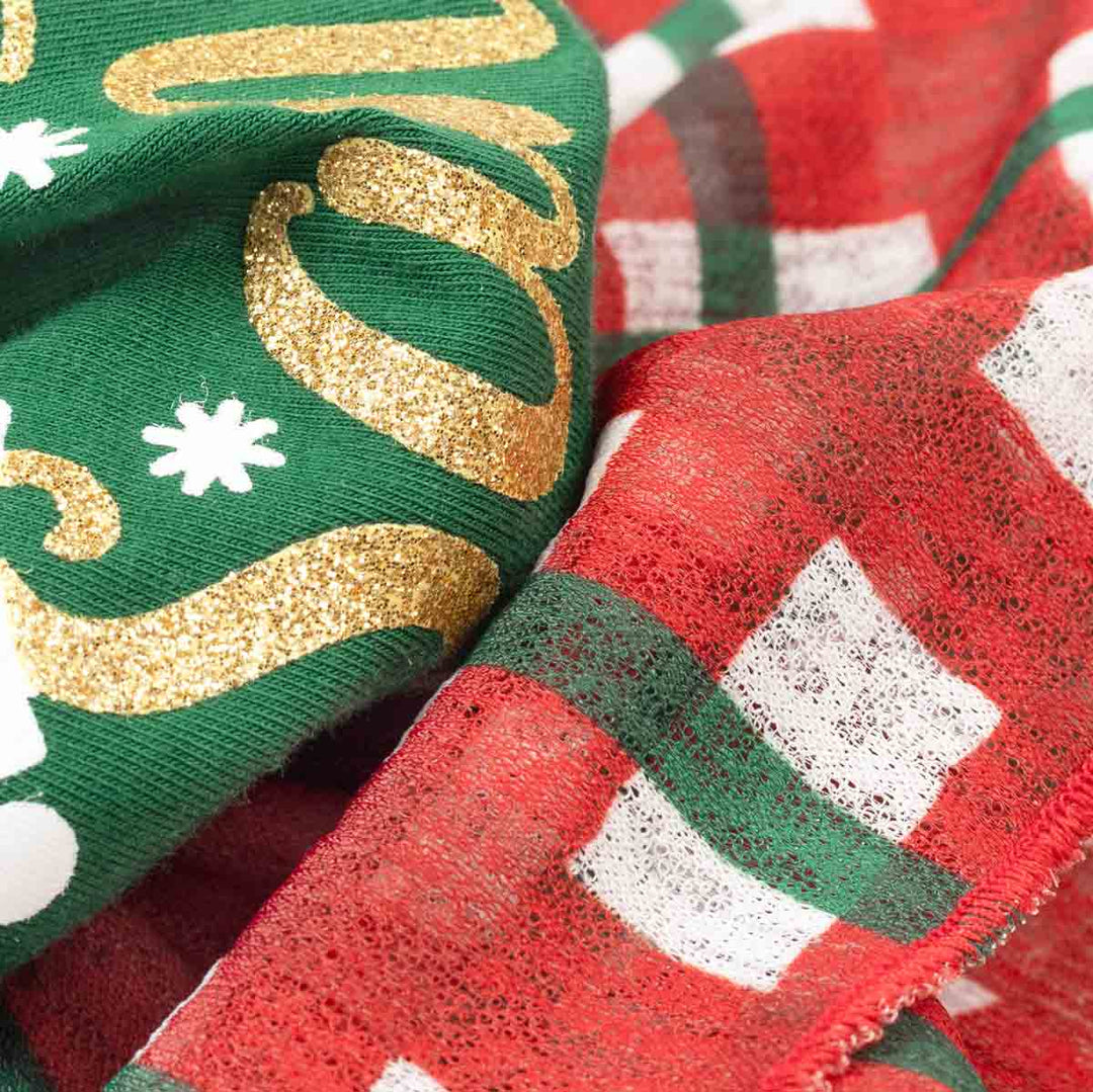 Close-up of fabric on dog Christmas tulle dress with a green knit section featuring gold glitter script and white snowflake motifs, layered over a red plaid fabric