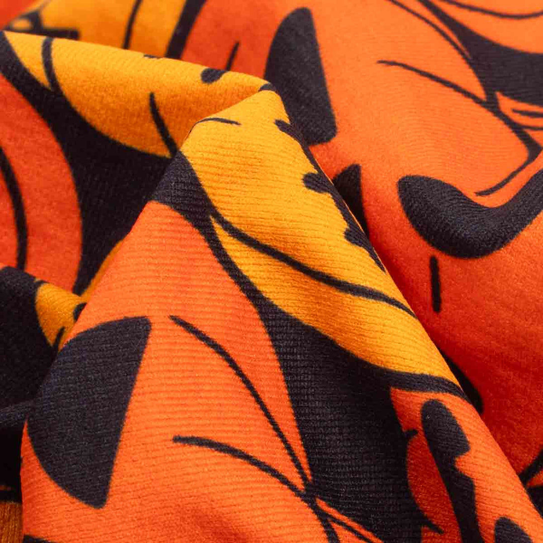 Close-up of a textured fabric with a bold orange and black abstract pattern, showing the material's weave and folds
