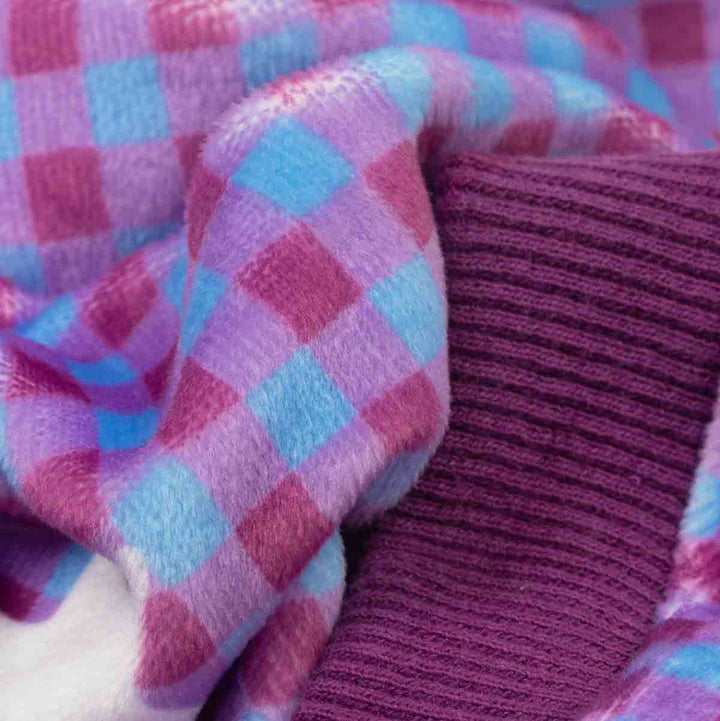 A close-up of soft plush fabric in a pink, purple, and light blue check pattern, layered over a ribbed knit fabric in deep purple