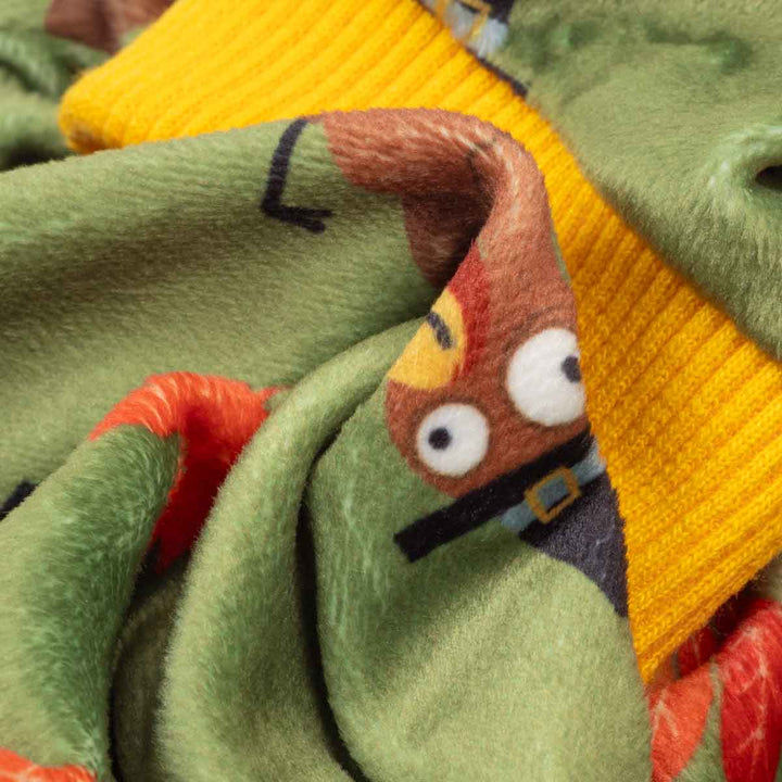 Close-up of a fleece dog pjs featuring a cartoon turkey character peeking out from behind a bright yellow ribbed knit collar, with green and orange-red accents