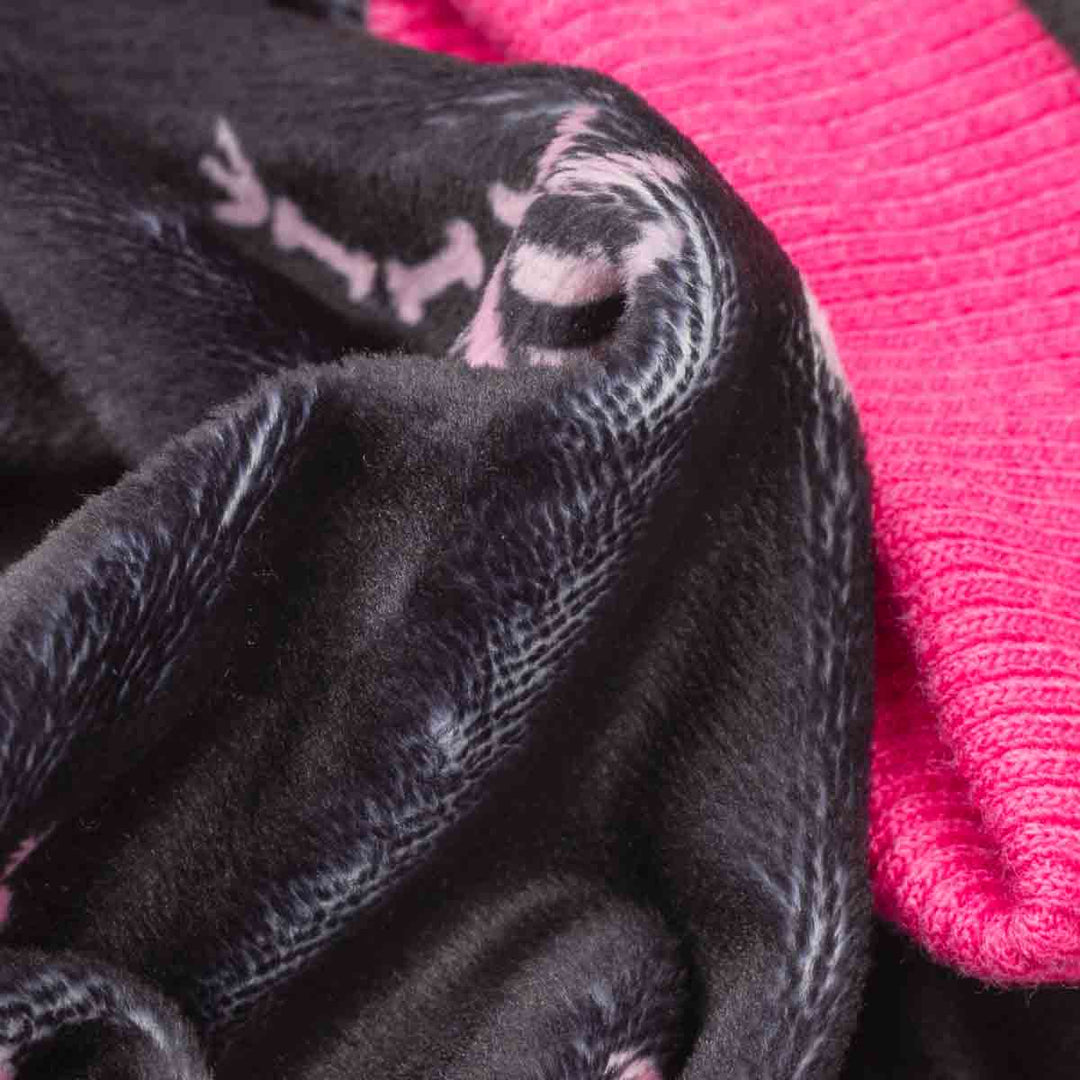 Close-up of a black plush dog fleece pajamas with a subtle white pattern, layered over a bright pink ribbed knit fabric