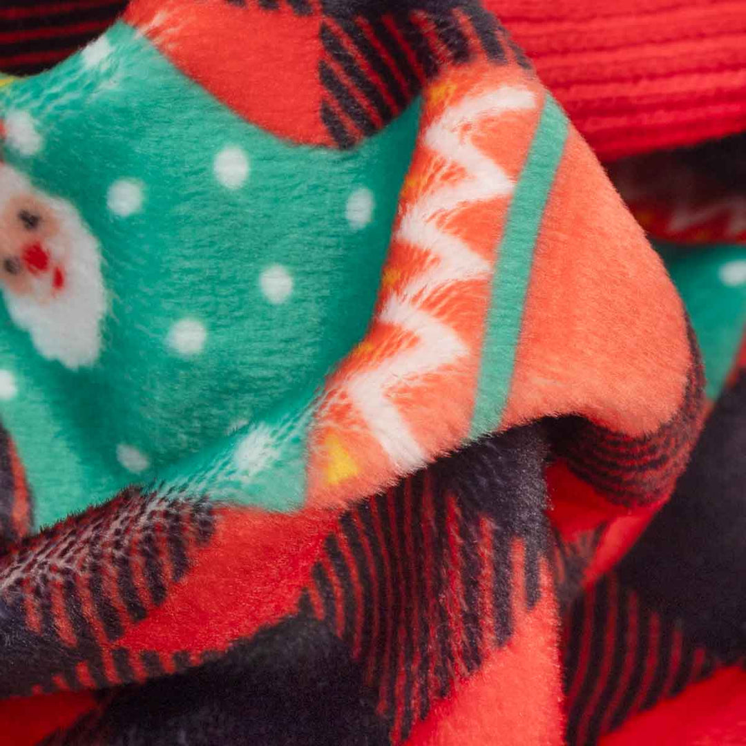 Close-up of a plush fleece fabric on dog Chrsitmas onesie with a festive pattern, featuring red and black buffalo plaid, a green sock with white polka dots and a Santa face, and orange and white chevron details
