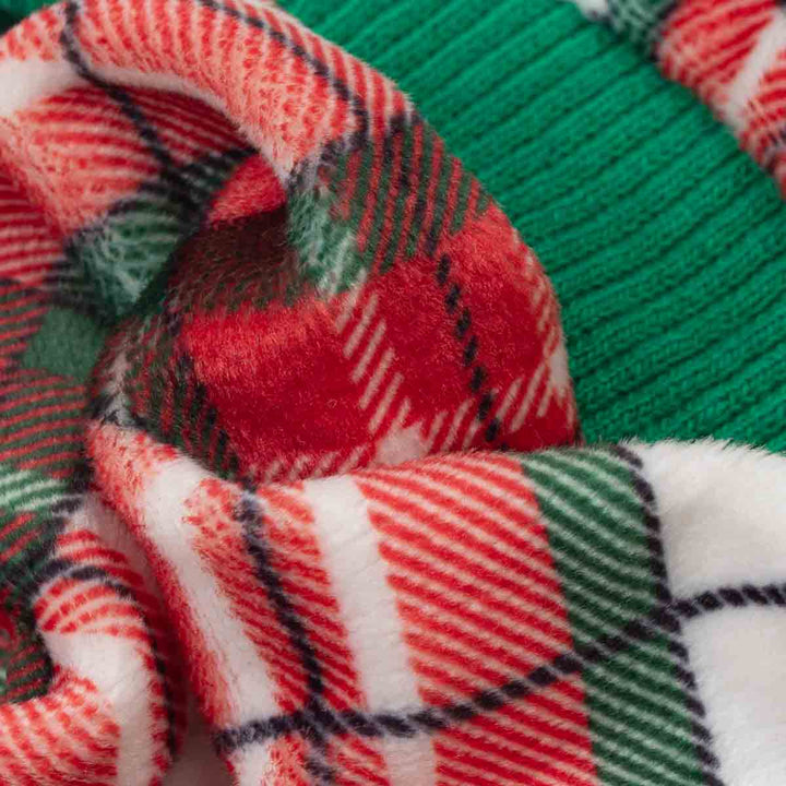 Close-up of a cozy fleece fabric of dog Christmas onesie with a festive holiday plaid pattern in red, green, white, and thin black lines, draped over a ribbed green knit fabric