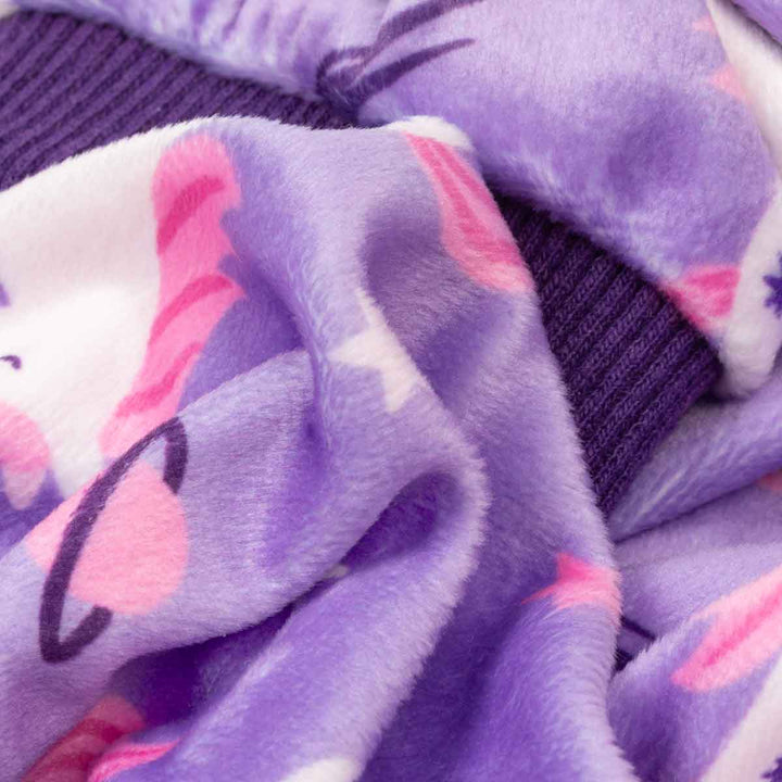 Close-up of a dog fleece pajamas with a purple, pink, and white unicorn pattern, paired with a dark purple ribbed cuff