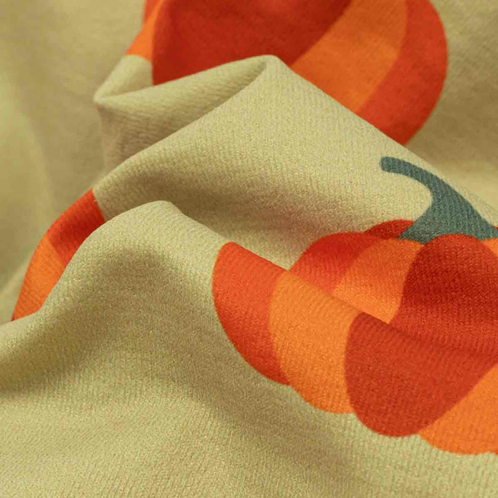 Close-up of a festive dog tshirt's soft fabric with a repeating pumpkin print in orange, red, and teal on a light beige background