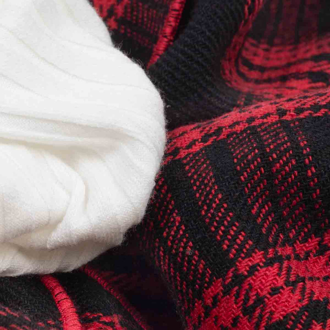 Close-up of soft white ribbed fabric on pet sweater dress with red plaid trim detail.