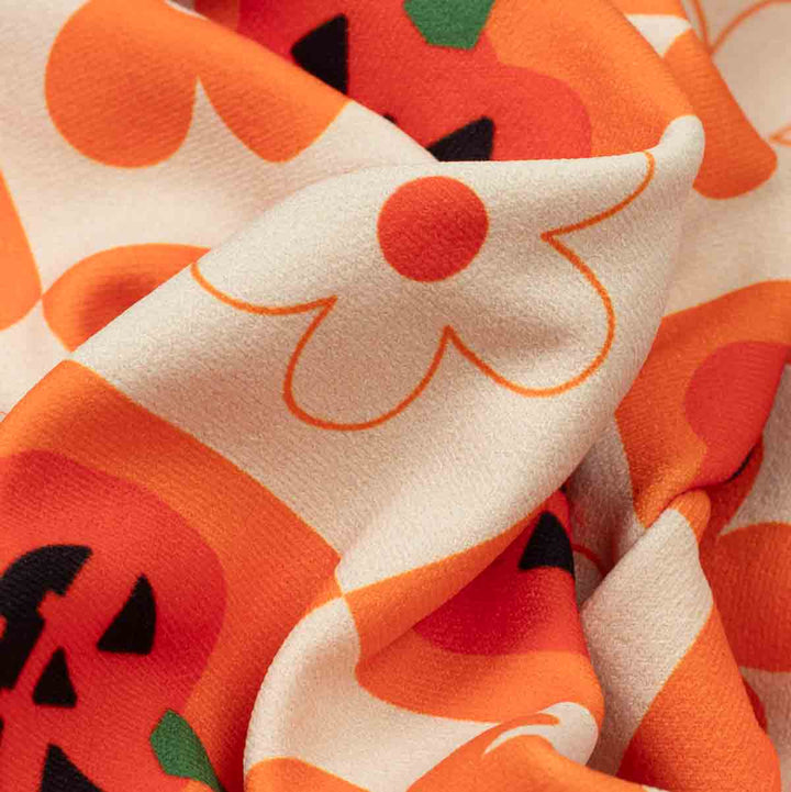 Close-up of a soft fabric with flower and pumpkin pattern featuring orange and cream blocks