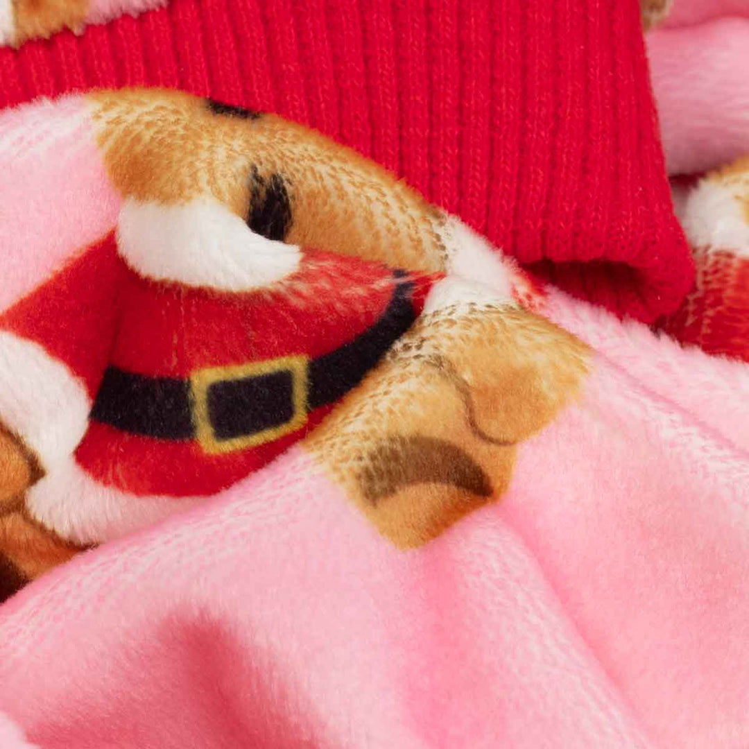 Close-up of plush dog Christmas pajama fabric featuring a teddy bear dressed in a Santa hat, layered over bright pink fleece and a red ribbed knit cuff