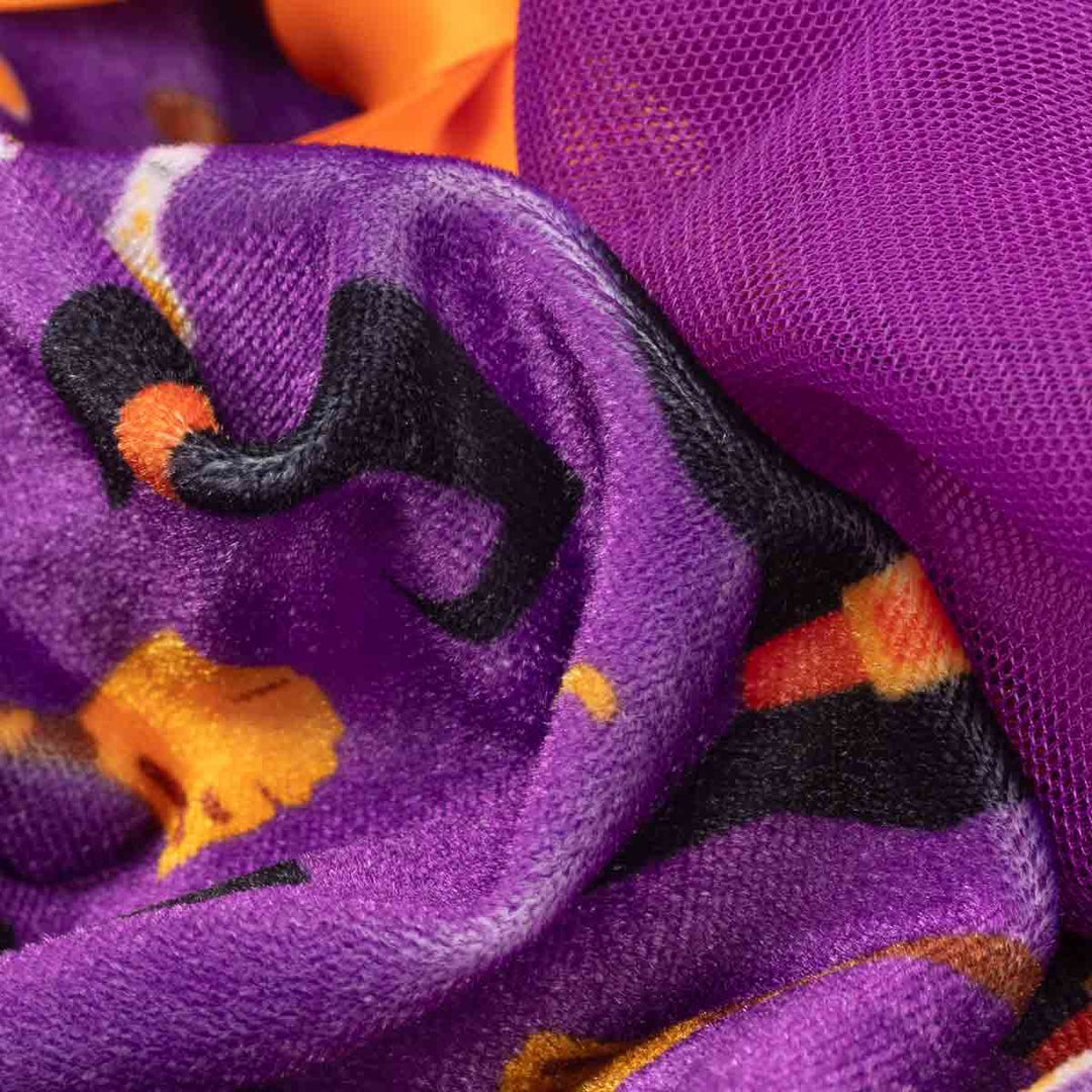 Close-up of a purple dog Halloween dress featuring a Halloween-themed print with black bats, orange pumpkins, and a sheer purple mesh lining