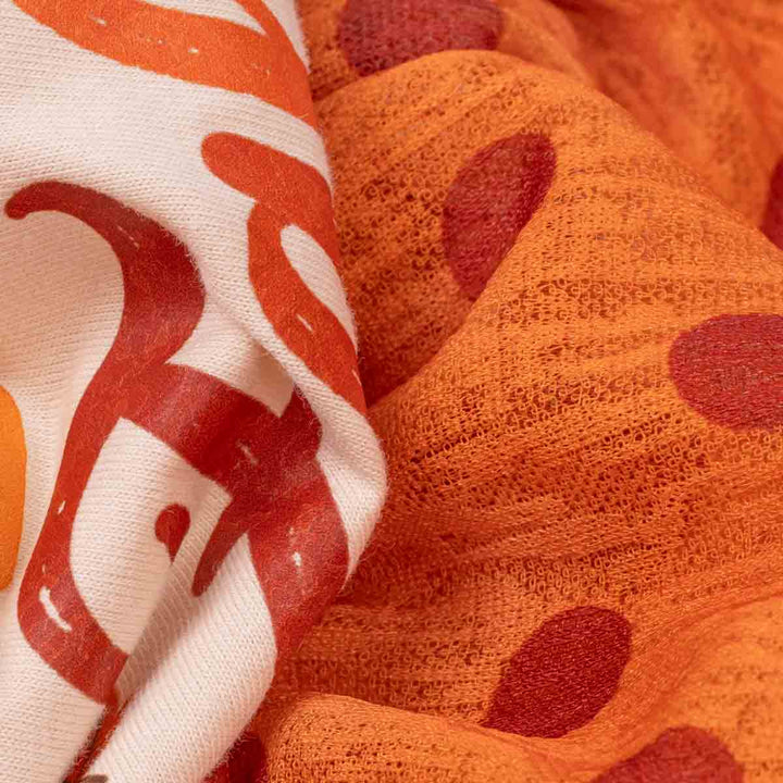 Close-up of a textured knit fabric with two patterns: one orange with dark red polka dots, and another off-white with bold orange and red abstract shapes