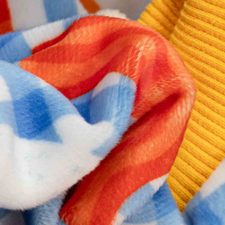 Close-up of a soft plush fabric on dog onesie with blue, white, and orange sections, next to a yellow ribbed knit fabric