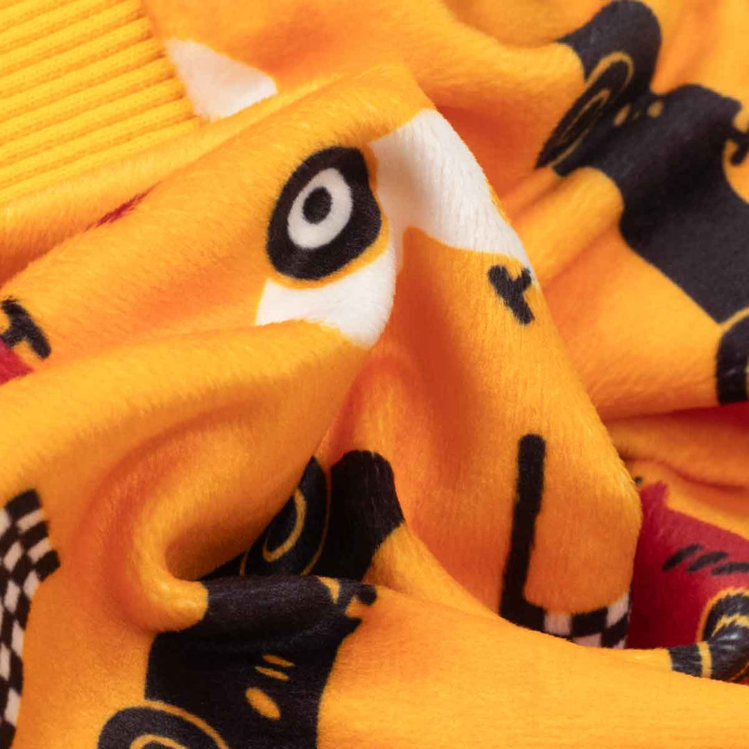 Close-up of a plush fabric product in bright yellow-orange with a cartoon race car pattern in black, white, and red