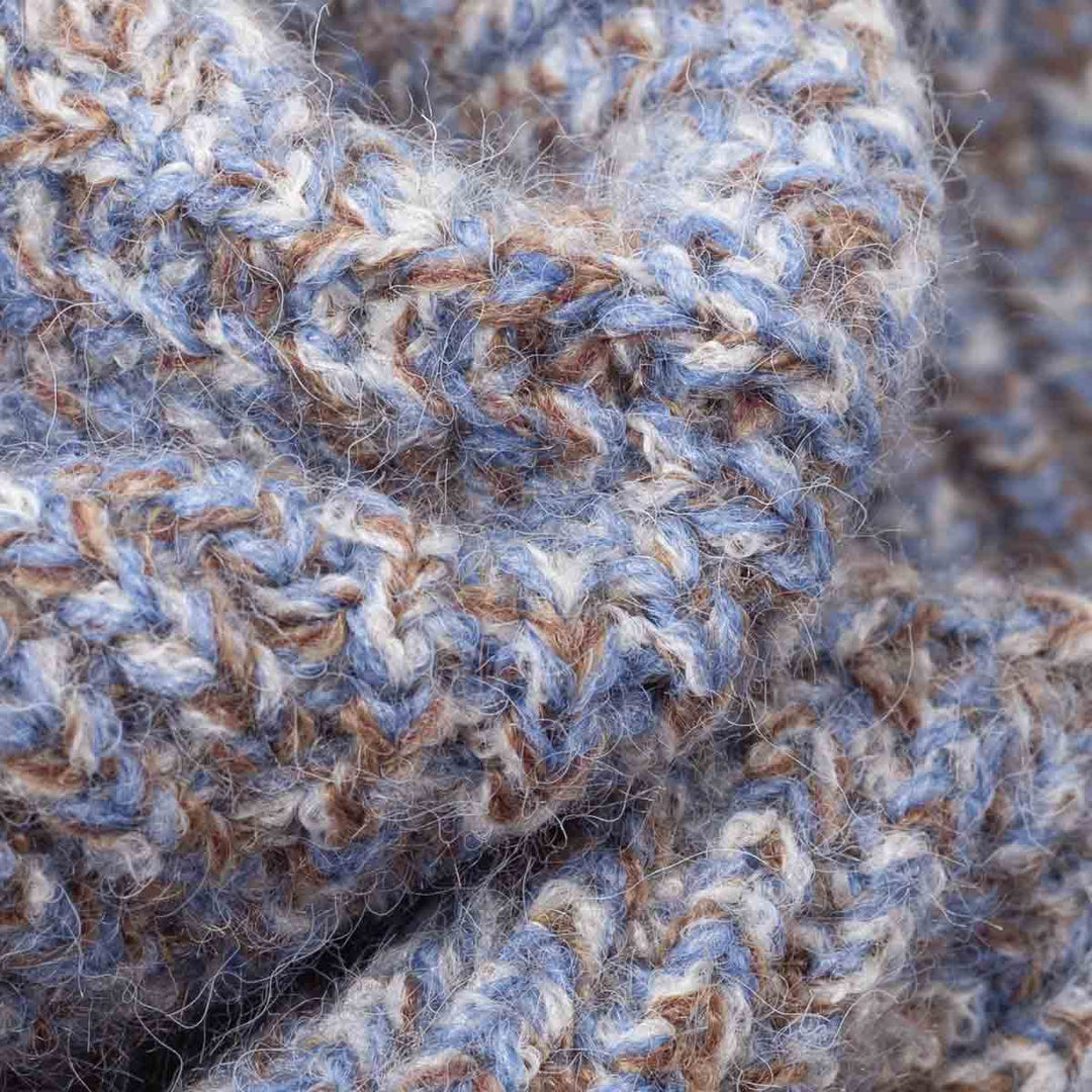 Close-up of a chunky knit fabric with a heathered pattern of dusty blue, warm brown, and off-white yarn