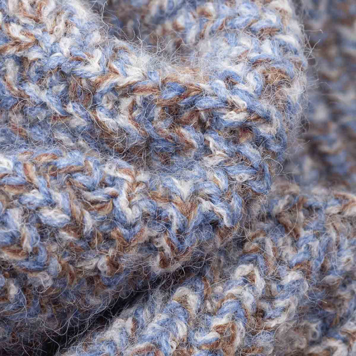 Close-up of a chunky knit fabric with a heathered pattern of dusty blue, warm brown, and off-white yarn
