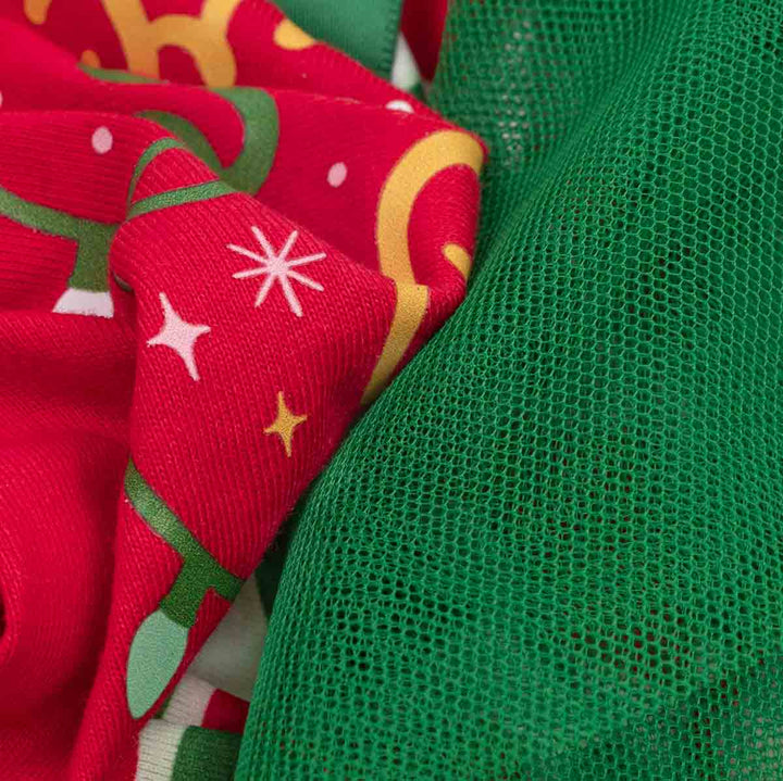 Close-up of two fabric textiles: one bright red with green and yellow holiday tree and star patterns, and one solid green mesh-like fabric, overlapping in a detailed texture shot
