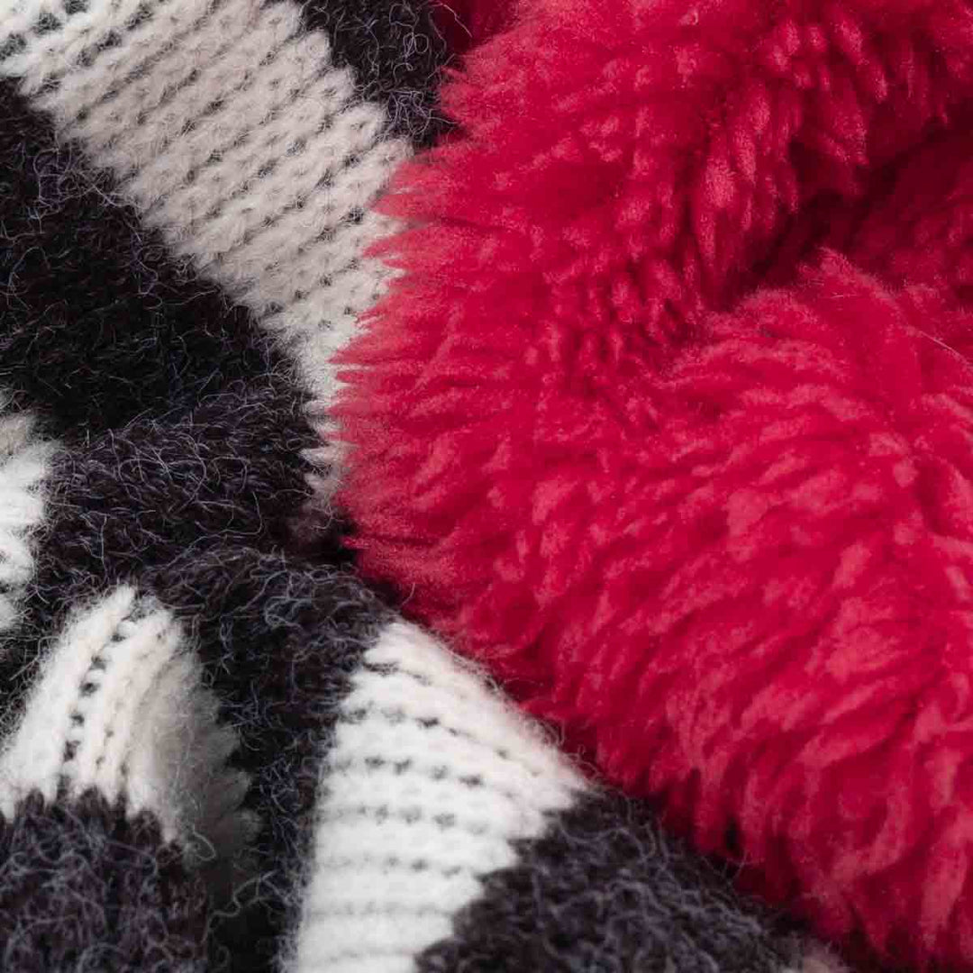 Close-up of a plush knit dog sweatshirt showing a bright red sherpa-like section layered over a black, and white striped knit fabric.