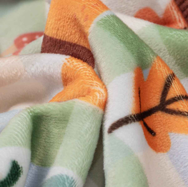 Close-up of a plush fleece dog pajamas with a colorful autumn pattern featuring orange leaves, green stripes, and brown accents on a white background