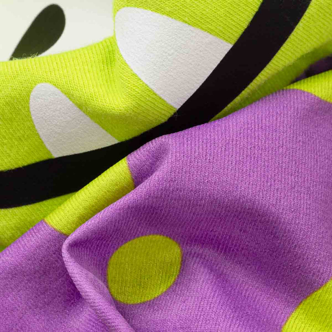 Close-up of a knit fabric with a bold graphic pattern in bright lime green, lavender purple, white, and black