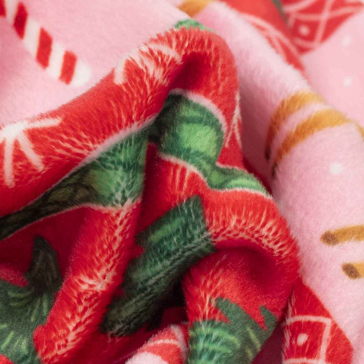 Close-up of a plush fleece fabric of Christmas dog pjs with a holiday pattern, featuring red and green holiday prints on a light pink background