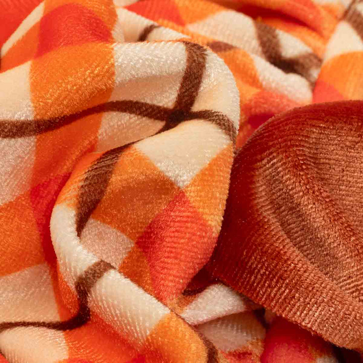 Close-up of a plush fleece dog winter dress with a warm autumn plaid pattern in orange, cream, and brown