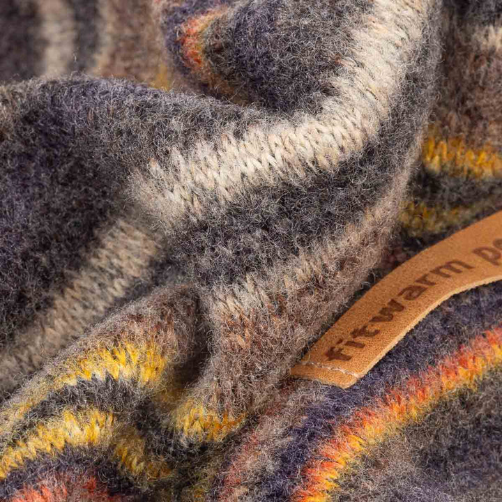 Close-up of a soft, fuzzy knit fabric with a plaid pattern in gray, beige, yellow, orange, and dark blue, featuring a tan leather brand tag that reads 'fitwarm'