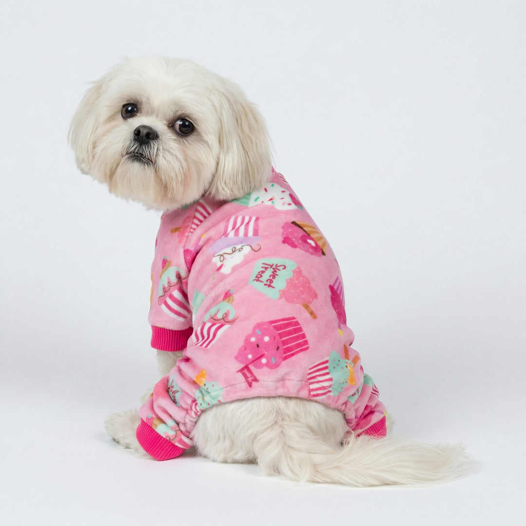 White dog sitting in pink dog pajamas featuring colorful cupcake prints