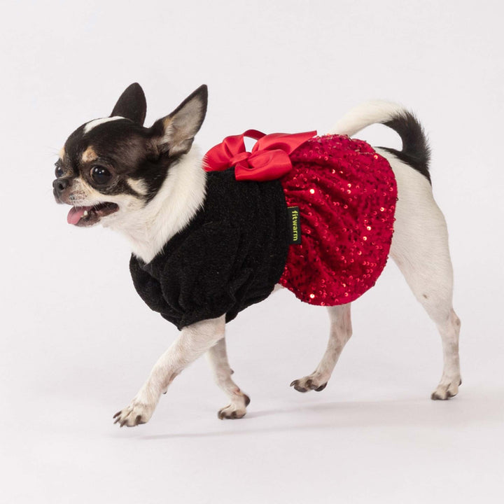 Tiny dog posing in a decorative Christmas dog dress with red sequins and a bold bow