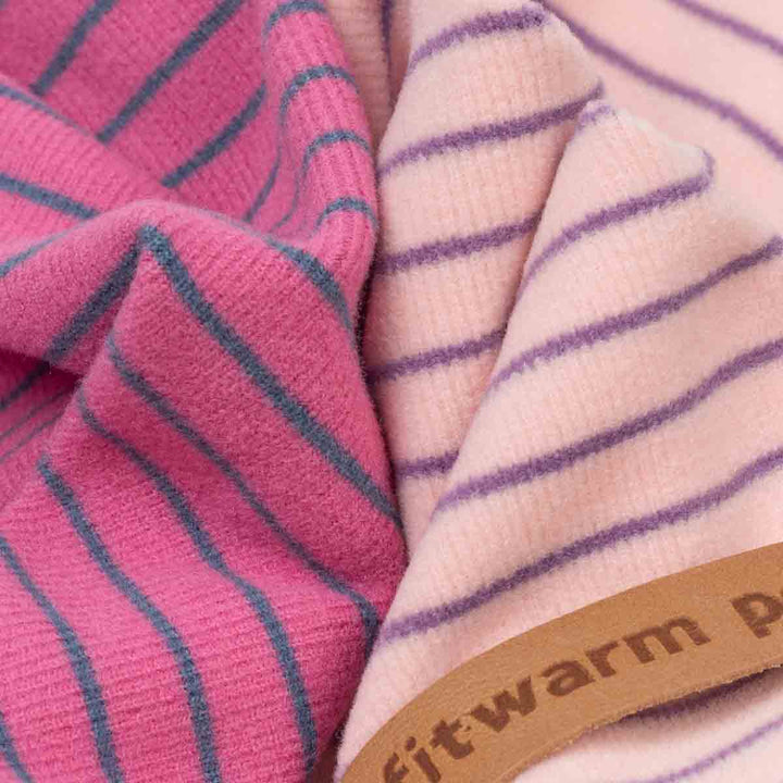 Close-up of two soft striped knit fabrics of dog pajamas, one in pink with teal stripes and one in pale pink with purple stripes