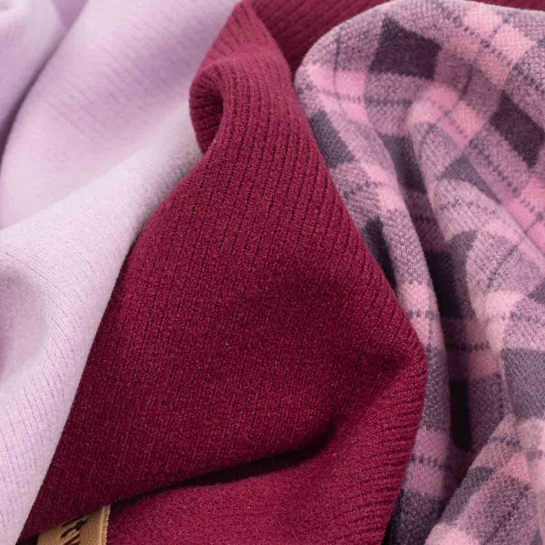 Close-up of folded knit fabric in multiple colors, including a deep burgundy ribbed knit, a pale pink plaid pattern, and a light lavender knit