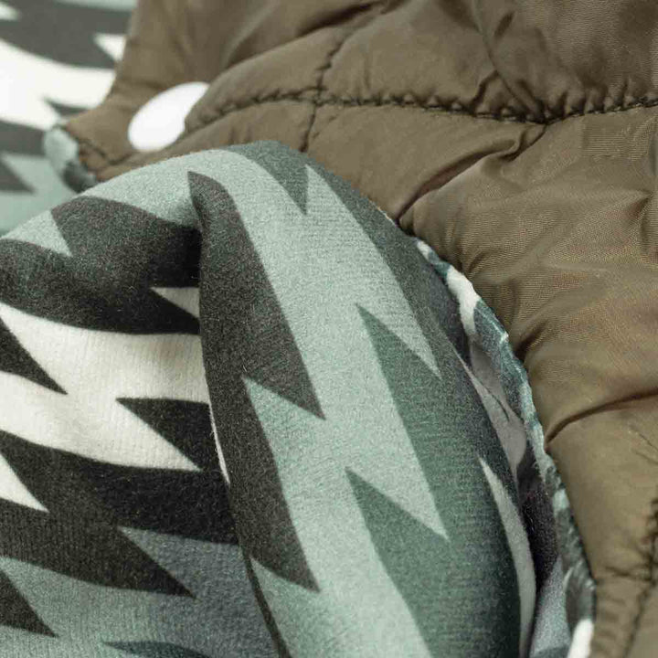 Close-up of a quilted olive dog coat with a gray, black, and white geometric patterns