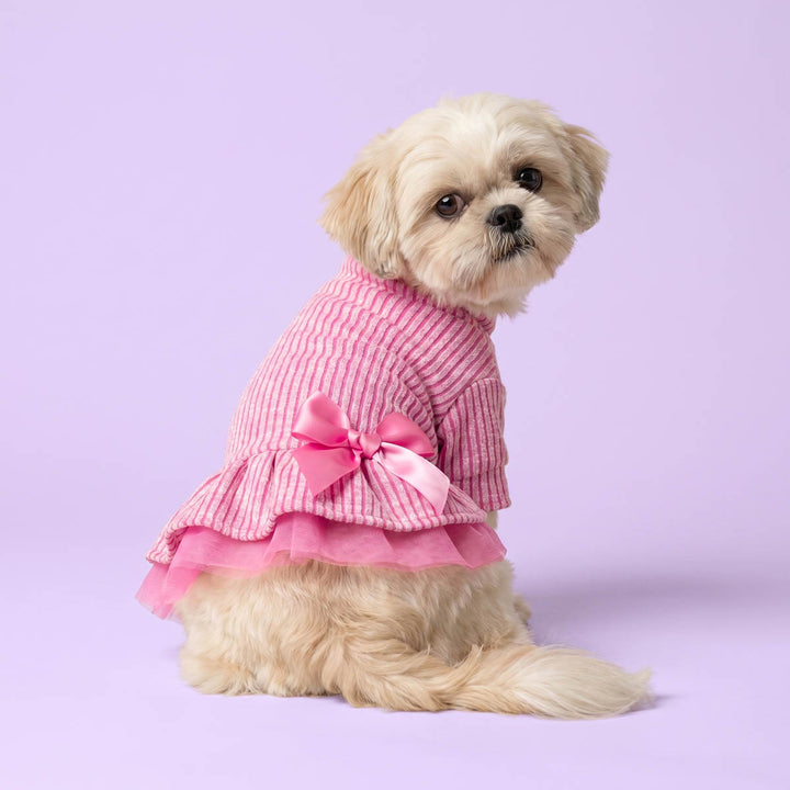 Dog wearing a pink dog dress with a bow on a light purple background