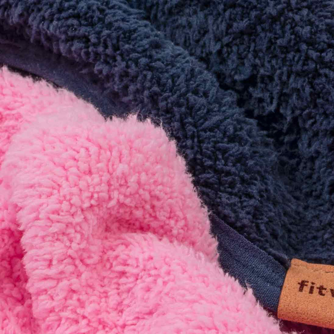 Close-up of a fleece dog winter sweaters in two colors: a bright pink layer and a dark navy blue layer, with a small tan fabric brand tab visible on the edge