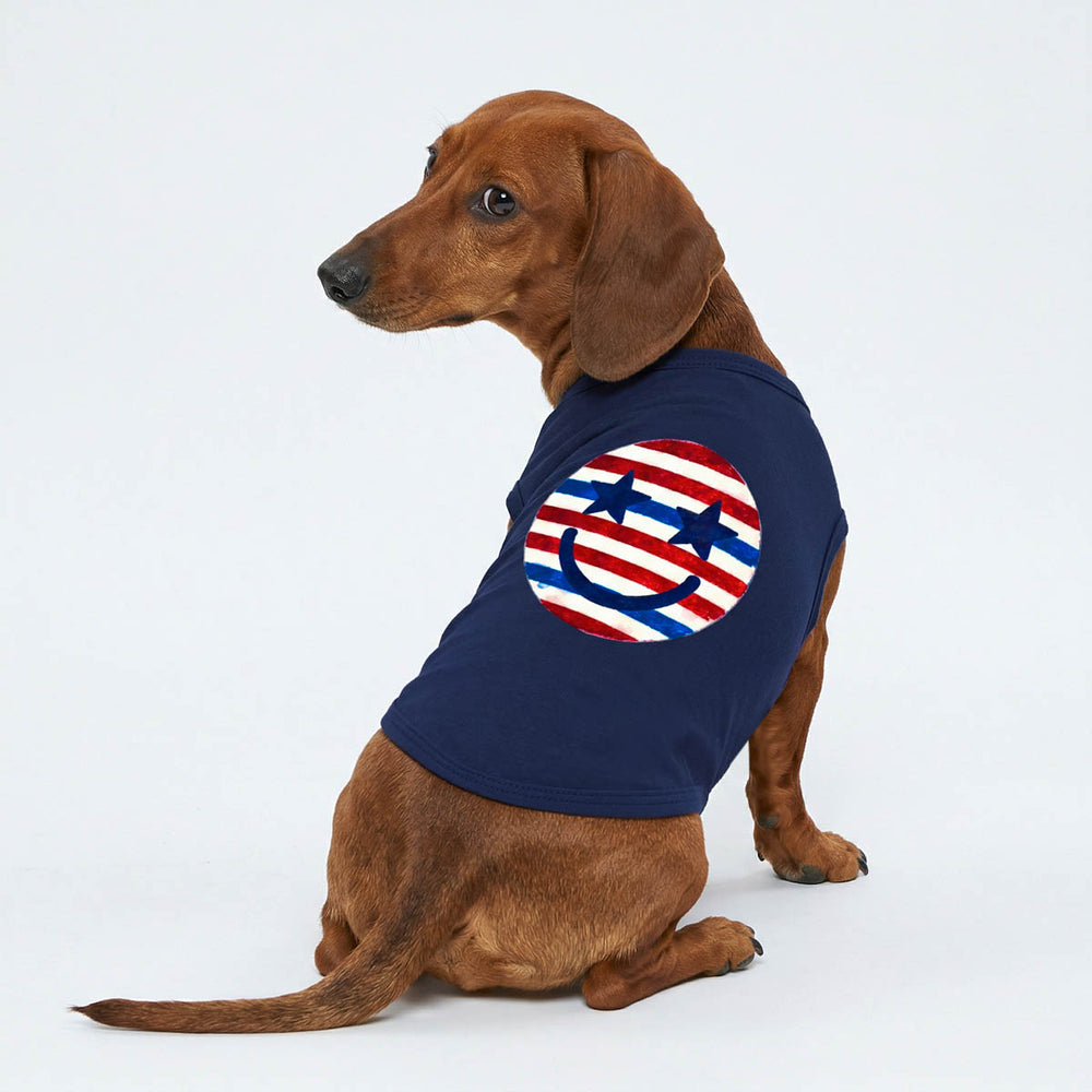 Dog wearing a navy blue dog t-shirt with a red, white, and blue striped smiley face design on a white background