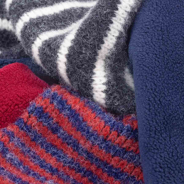 Close-up of soft fleece fabric in multiple colors and patterns, including navy blue, gray and white stripes, red and blue stripes, and solid red