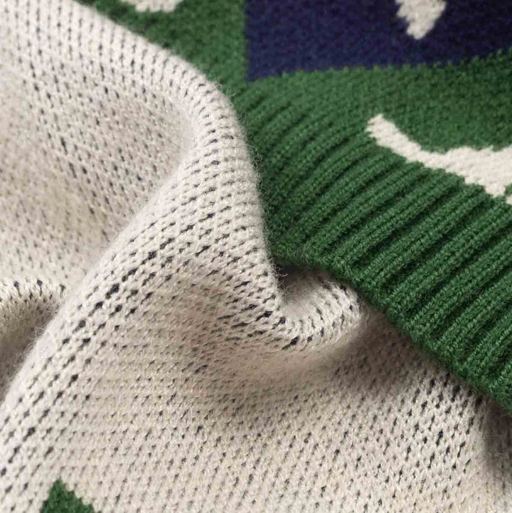 Close-up of a knit textile with a cream and green pattern, showing the texture of the knit fabric and a ribbed green border