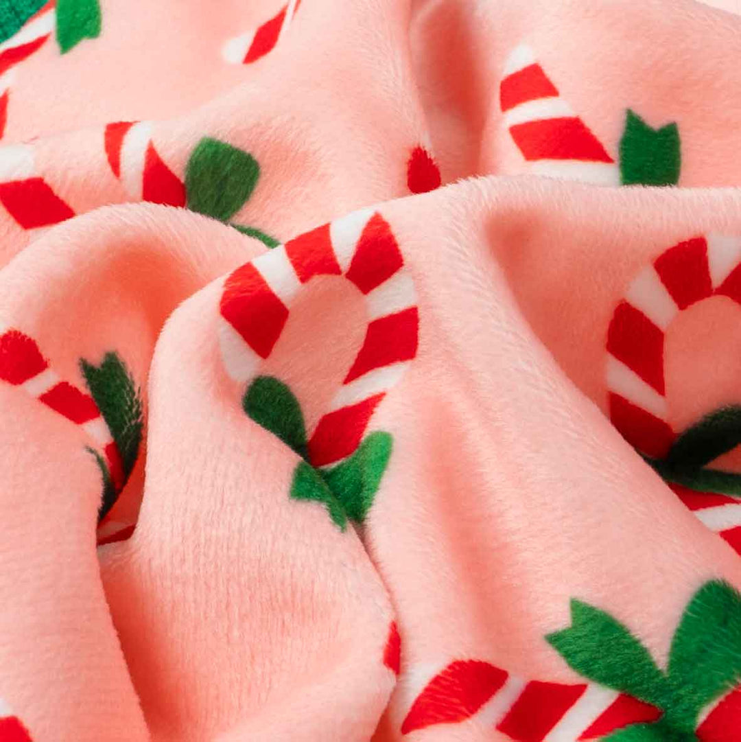 Close-up fabric detail of Christmas dog pajamas with red candy cane and green bow prints.