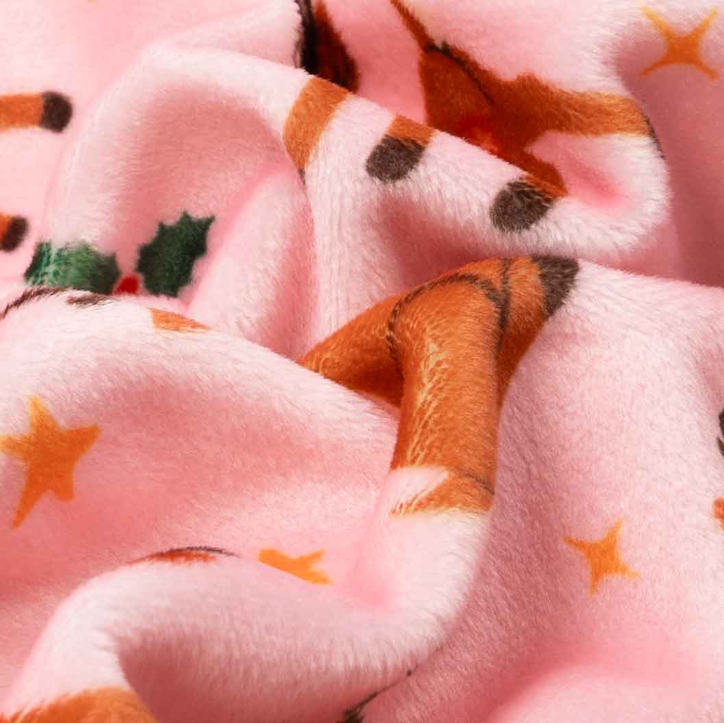 Close-up fabric detail of Christmas dog pajamas in pink with reindeer and star prints.