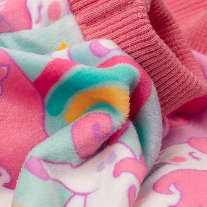 Close-up of soft, plush dog pajamas with a pastel rainbow, unicorn, and star print and pink ribbed cuffs.