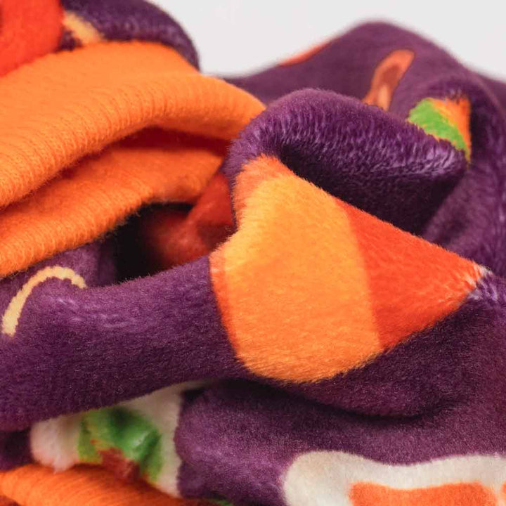 Plush purple Halloween dog pajamas featuring candy corn, jack-o'-lantern, and swirl prints, orange cuff.