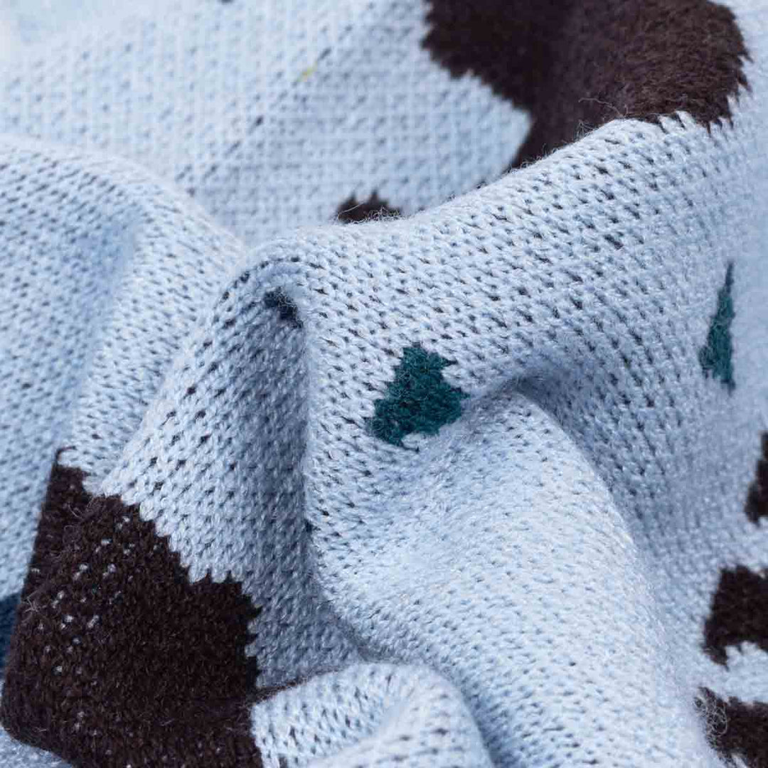 Close-up of a knitted dog winer sweater fabric in pale icy blue with dark brown patches and small teal tree-like motifs