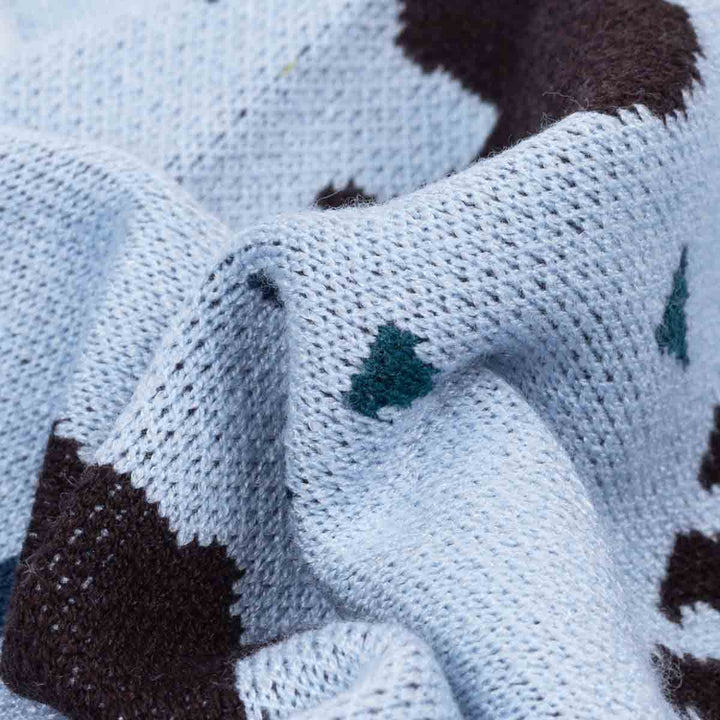 Close-up of a knitted dog winer sweater fabric in pale icy blue with dark brown patches and small teal tree-like motifs