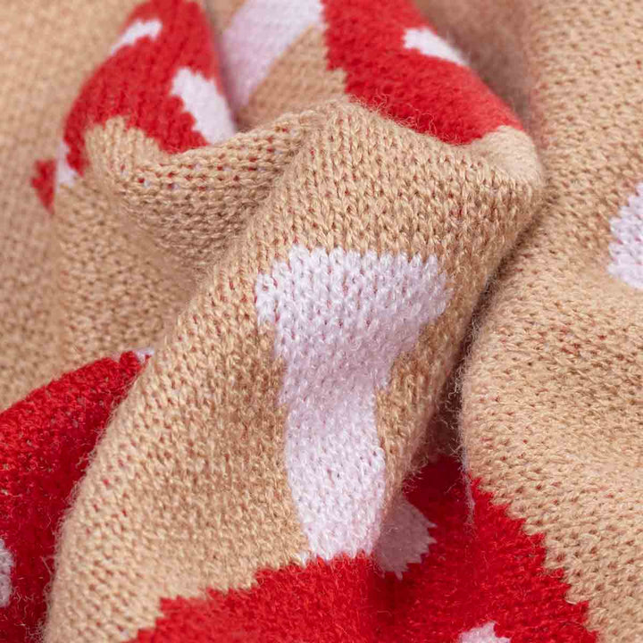 Close-up of a knitted textile with a beige base and red and white mushroom pattern